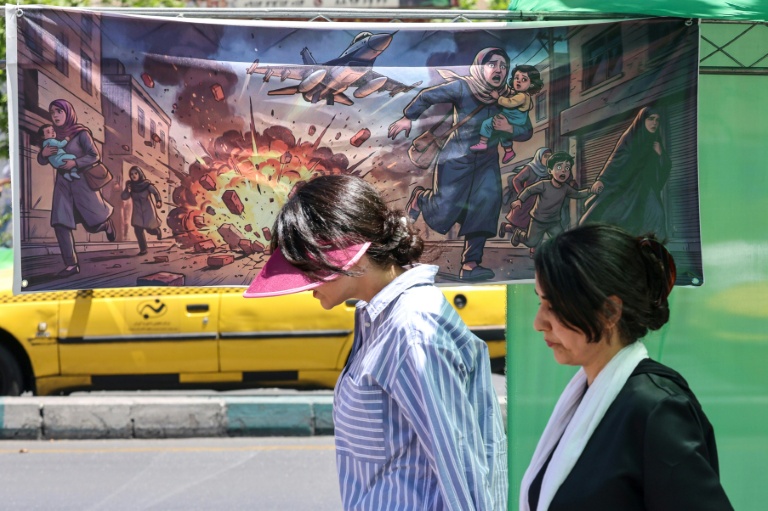 Des Iraniennes passent devant une affiche représentant les frappes israélo-américaines contre l'Iran, le 9 mai 2026 à Téhéran 