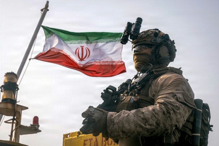 Cette photographie fournie par le Corps des Marines des États-Unis, prise le 16 juillet 2026 par le service des relations publiques du Commandement central américain, montrerait un drapeau iranien flottant derrière un marine américain de la 11e Unité expéditionnaire des Marines, dans le Golfe.