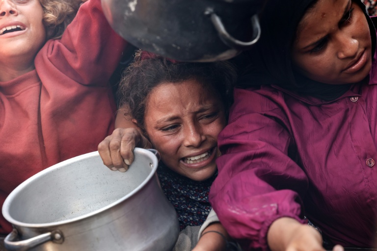 Des enfants palestiniens tendent leurs casseroles vides devant une cuisine communautaire à Khan Younes, dans le sud de la bande de Gaza, le 21 août 2025