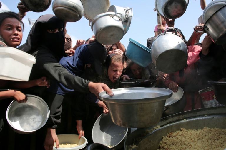 Des femmes et des enfants palestiniens tendent leurs casseroles vides devant une cuisine communautaire à Khan Younes, dans le sud de la bande de Gaza, le 21 août 2025