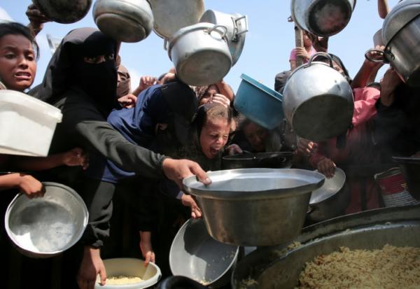Des femmes et des enfants palestiniens tendent leurs casseroles vides devant une cuisine communautaire à Khan Younes, dans le sud de la bande de Gaza, le 21 août 2025