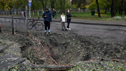 Des personnes se tiennent près d'un cratère causé par un missile, à proximité d'une école endommagée à la suite d'une attaque russe à Kiev, le 19 octobre 2026