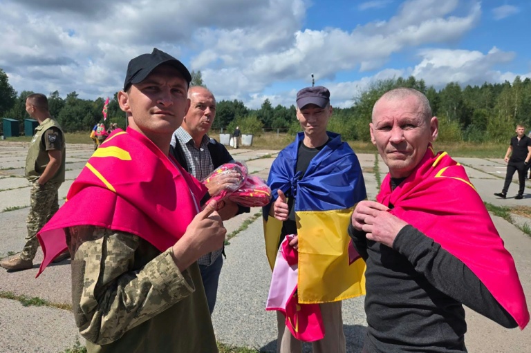 Photo diffusée par le Quartier général de coordination pour le traitement des prisonniers de guerre, le 19 août 2026, montrant d'anciens prisonniers de guerre ukrainiens, enveloppés dans des drapeaux nationaux, près d'un bus après un échange effectué dans un lieu tenu secret