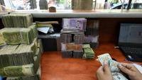 Un employé compte des dollars américains devant une pile de livres syriennes dans un bureau de change à Damas, le 21 mai 2025 en Syrie