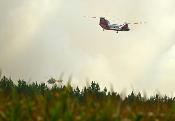 Un hélicoptère bombardier d'eau CH-47D Chinook du Rural Fire Service (RFS) de Nouvelle-Galles du Sud (Australie) et un hélicoptère de la Sécurité civile française survolent la forêt de Luglon lors d'un incendie de forêt, le 14 août 2026 dans les Landes