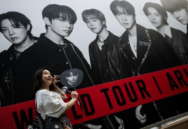 Une fan du groupe sud-coréen de K-pop BTS pose devant une affiche du groupe le 17 avril 2026 à Tokyo