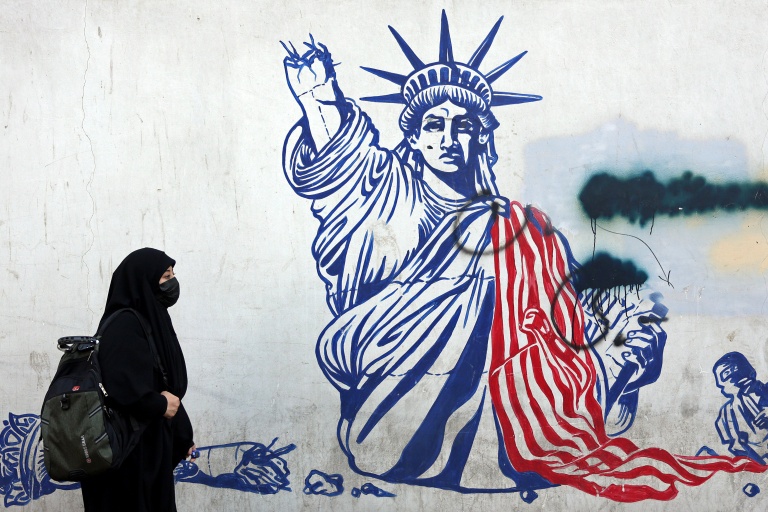 Cette photo, prise le 26 février 2026, montre une Iranienne voilée passant devant une fresque anti-américaine située à côté de l'ancienne ambassade des États-Unis à Téhéran.