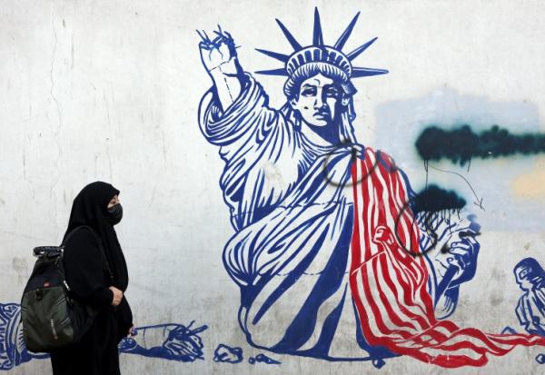 Cette photo, prise le 26 février 2026, montre une Iranienne voilée passant devant une fresque anti-américaine située à côté de l'ancienne ambassade des États-Unis à Téhéran.