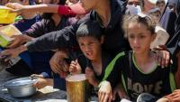 Des enfants palestiniens font la queue pour obtenir un repas chaud lors d'une distribution assurée par une cuisine soldiaire au camp de réfugiés de Nousseriat, dans le centre de la bande de Gaza, le 5 mai 2025