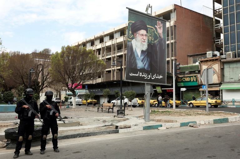Des membres des forces de sécurité iraniennes montent la garde dans une rue de Téhéran, près d'un panneau d'affichage à l'effigie du guide suprême iranien, l'ayatollah Ali Khamenei, le 2 mars 2026.