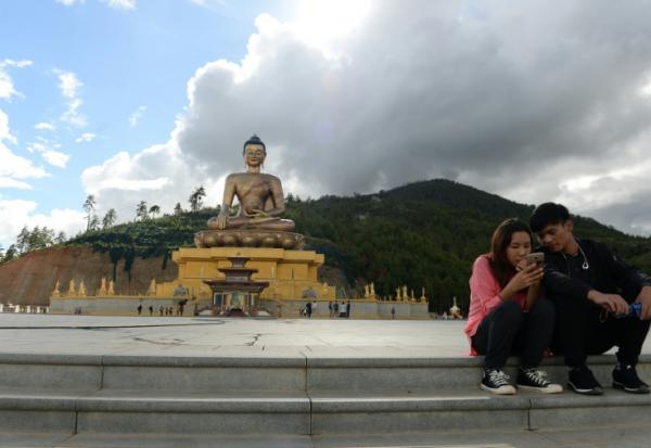 Un couple assis regarde l'écran d'un téléphone portable à côté d'une statue de Bouddha à Thimphou, la capitale du Bouthan, le  25 août 2018