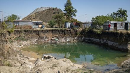 Des habitations surplombent une fosse à ciel ouvert creusée par des mineurs illégaux à la recherche de chrome à Bapong, un village minier de la province du Nord-Ouest (Afrique du Sud), le 25 août 2026