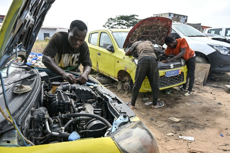 Des mécaniciens informels travaillent sur des moteurs de voiture dans le quartier d'Angré, à Abidjan, la capitale économique ivoirienne, le 21 juillet 2026.