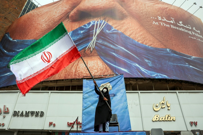 Une femme agite un drapeau iranien devant un panneau anti-américain en référence à Donald Trump et à la fermeture du détroit d'Ormuz, le 5 mai 2026 à Téhéran