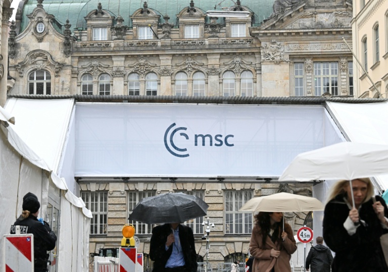 Des gens s'abritent de la pluie en passant devant un accès à la Conférence de Munich sur la sécurité (MSC), le 12 février 2026 à Munich