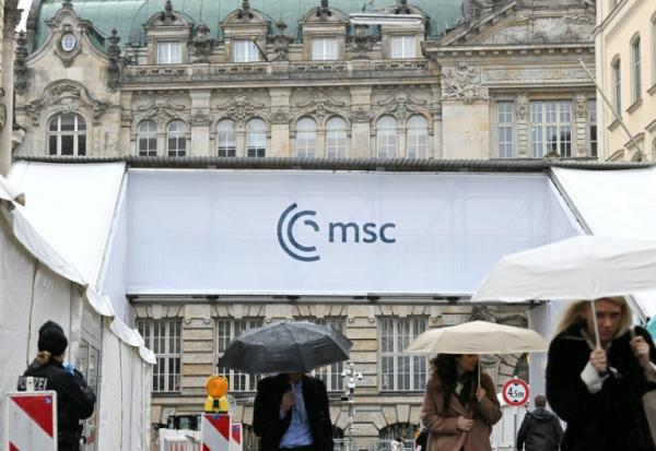 Des gens s'abritent de la pluie en passant devant un accès à la Conférence de Munich sur la sécurité (MSC), le 12 février 2026 à Munich