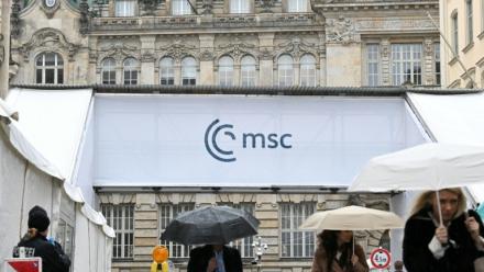 Des gens s'abritent de la pluie en passant devant un accès à la Conférence de Munich sur la sécurité (MSC), le 12 février 2026 à Munich