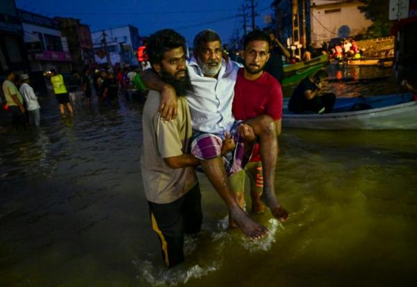 De jeunes hommes portent une personne âgée dans une rue inondée de Wellampitiya, dans les faubourgs de Colombo, la capitale du Sri Lanka, le 30 novembre 2025