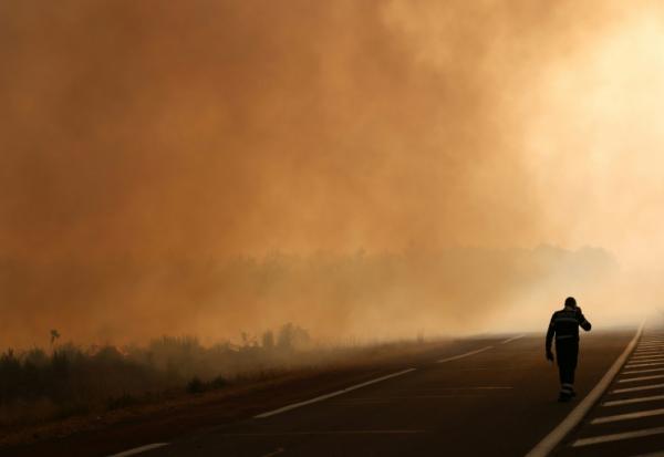 Un pompier marche sur une route en bordure d'une zone en feu à Ares, le 26 juillet 2026, alors qu'un incendie ravage la forêt au nord du bassin d'Arcachon en Gironde depuis le 22 juillet