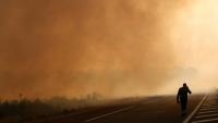 Un pompier marche sur une route en bordure d'une zone en feu à Ares, le 26 juillet 2026, alors qu'un incendie ravage la forêt au nord du bassin d'Arcachon en Gironde depuis le 22 juillet
