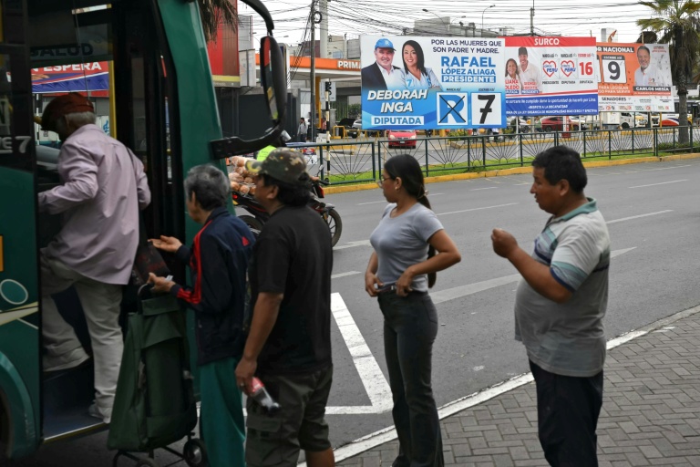 Des personnes montent dans un bus près d'affiches de campagne à Lima, le 11 avril 2026
