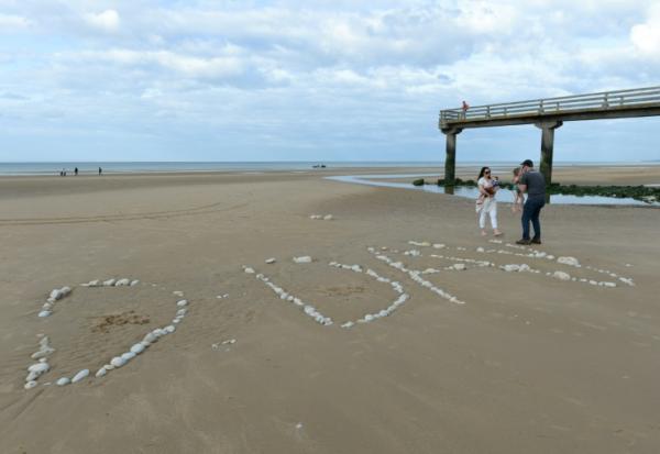 Une famille sur "Omaha Beach", où le mot "D-Day" a été tracé à l'aide de galets, à  Vierville-sur-Mer, dans le Calvados, lors des célébrations du 75e anniversaire du Débarquement en juin 2019