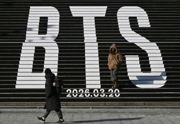 Des piétons le long d'escaliers décorés du logo du groupe de K-pop BTS, près de la place Gwanghwamun à Séoul, le 14 janvier 2026