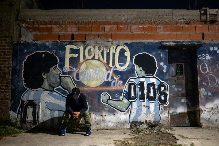 Un homme assis devant une fresque murale de Diego Maradona avec l'inscription 