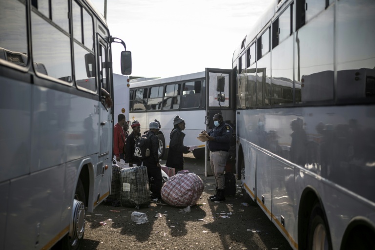 Un responsable sud-africain de l’immigration vérifie les noms de migrants en situation irrégulière faisant la queue pour monter dans des cars au Durban Drive-In, à Durban, le 29 juin 2026, en partance pour le Zimbabwe