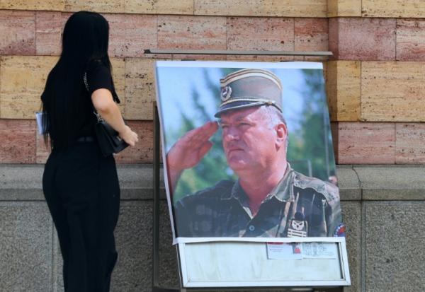 Une femme regarde un portrait de l'ancien chef militaire des Serbes de Bosnie, Ratko Mladić, devant la cathédrale orthodoxe de Banja Luka, en Bosnie, le 28 août 2026, au lendemain de sa mort à l'âge de 84 ans dans un hôpital pénitentiaire de La Haye