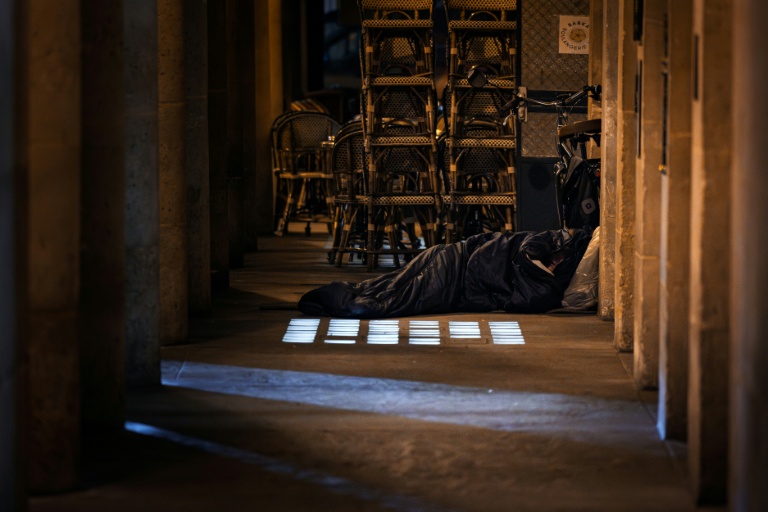 Un sans-abri dort dans un sac de couchage à côté de la terrasse d'un café à Paris, le 15 octobre 2025