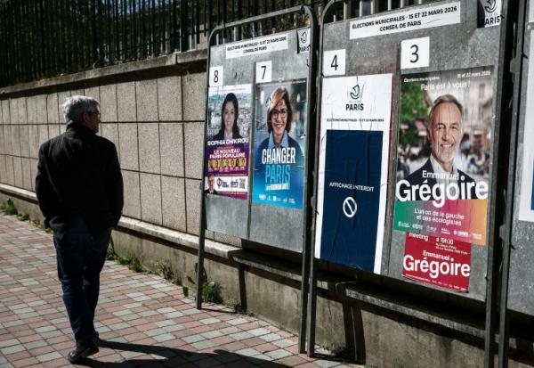 Une personne passe devant des affiches électorales pour les municipales, le 18 mars 2026 à Paris
