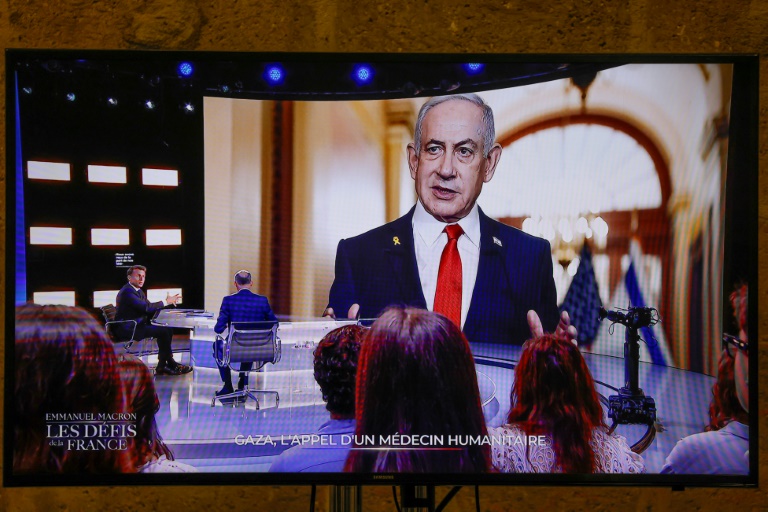 Cette photo prise sur un écran de TF1, montre le président français Emmanuel Macron, alors qu'une photo du Premier ministre israélien Benjamin Netanyahu s'affiche en arrière-plan, lors d'une émission télévisée à Saint-Denis, en France, le 13 mai 2025