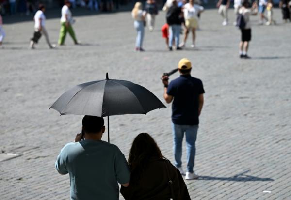 Des touristes visient Bruxelles à l'abri sous un parapluie pour se protéger du soleil lors d'une vague de chaleur le 27 mai 2026, en Belgique