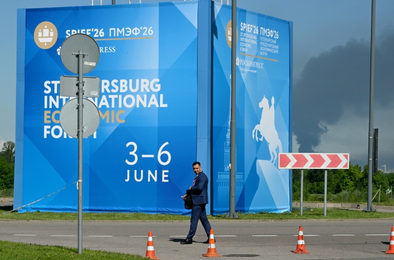 Un homme passe devant des affiches du Forum économique international de Saint-Pétersbourg alors que de la fumée s'élève en arrière-plan après des frappes de drones ukrainiens, le 3 juin 2026