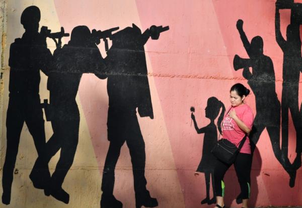 Une femme passe devant une fresque murale représentant des hommes armés visant des manifestants, allusion à la répression policière, dans une avenue de Tegucigalpa, le 27 novembre 2025
