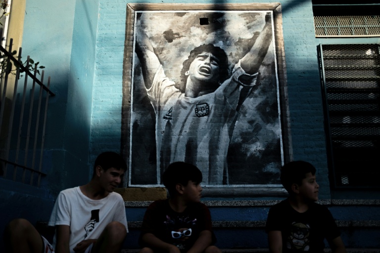Des garçons assis devant une fresque murale représentant la star du football Diego Maradona, décédé récemment, dans son quartier natal de Villa Fiorito, dans la province de Buenos Aires, en Argentine, le 9 avril 2026