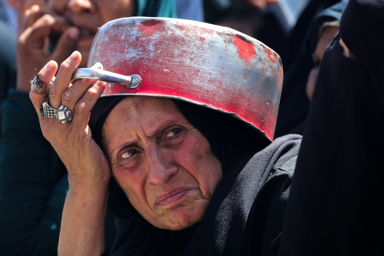 Une Palestinienne fait la queue pour recevoir un repas chaud à un point de distribution de nourriture dans le camp de réfugiés de Nousseirat, dans le centre de la bande de Gaza, le 24 mai 2025