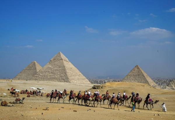 Des touristes à dos de chameau visitent la nécropole des pyramides de Gizeh, le 7 novembre 2025 en Egypte