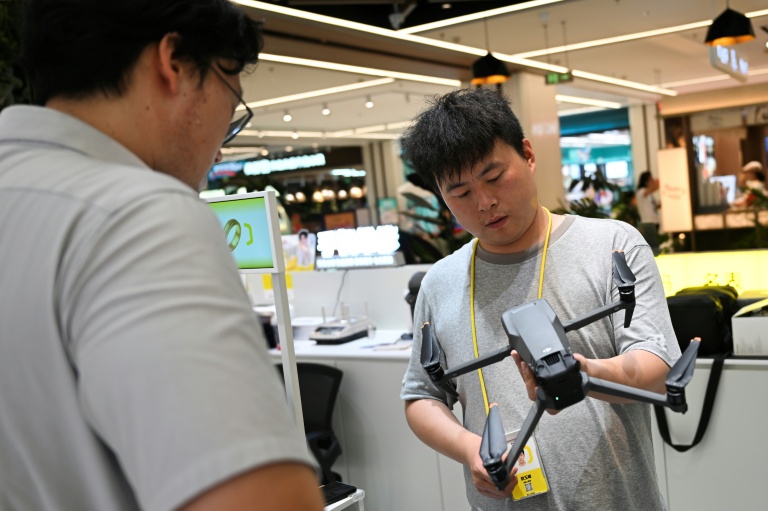 Un employé (à droite) d'un magasin dans un centre commercial inspecte un drone apporté par son propriétaire à Pékin le 16 septembre 2026.