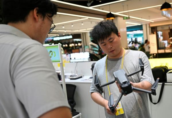 Un employé (à droite) d'un magasin dans un centre commercial inspecte un drone apporté par son propriétaire à Pékin le 16 septembre 2026.