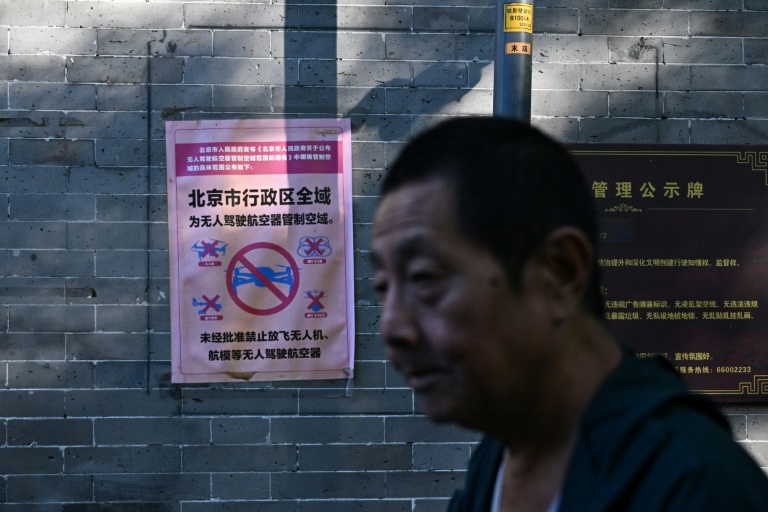 Un homme passe devant une affiche indiquant que l’ensemble de la zone administrative de Pékin constitue un espace aérien contrôlé pour les drones et autres aéronefs sans pilote, où tout vol est interdit sans autorisation, dans une ruelle de la capitale le 14 septembre 2026.
