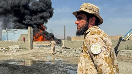 Un membre des forces de sécurité talibanes monte la garde alors que de la fumée s'élève du site de frappes aériennes pakistanaises sur des dépôts pétroliers, près de l'aéroport de Kandahar, le 13 mars 2026 en Afghanistan