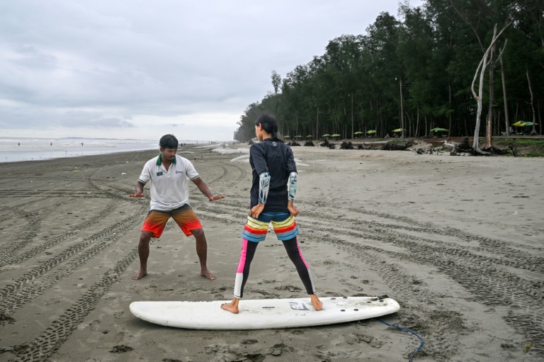 Mohammad Mannan (G) donne un cours de surf à un débutant, sur la plage de Cox's Bazar, dans le sud-est du Bangladesh, le 22 juin 2026  