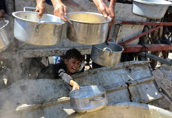 Un garçon palestinien tend une casserole vide devant une organisation de charité locale distribuant du riz cuit, dans la ville de Gaza, le 23 août 2025