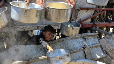 Un garçon palestinien tend une casserole vide devant une organisation de charité locale distribuant du riz cuit, dans la ville de Gaza, le 23 août 2025