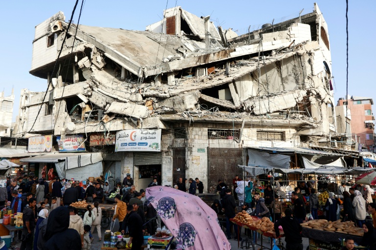 Des Palestiniens font leurs courses au pied d'un immeuble détruit du marché Zawiya, à Gaza, le 18 février 2026, aux premiers jours du mois sacré du Ramadan
