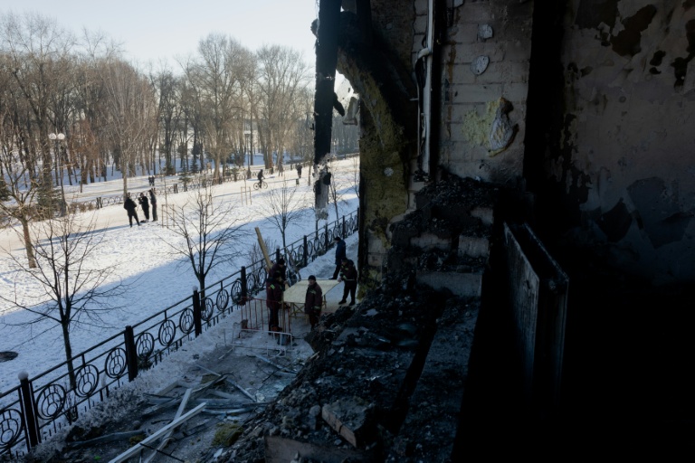 Des personnes apportent des planches pour boucher des fenêtres détruites après l'attaque par des drones d'une clinique privée à Kiev, le 5 janvier 2026, en Ukraine