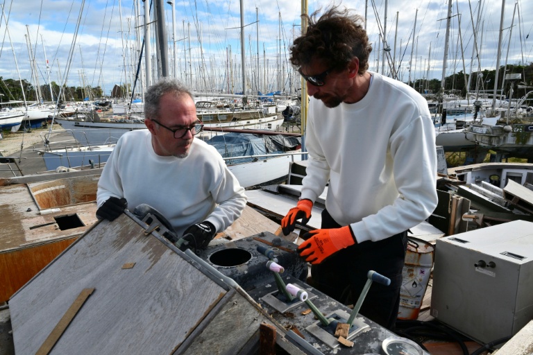 Thomas Bekkers (G) et Guillaume Delaunay cherchent des pièces réutilisables ou recyclables pour leur ressourcerie spécialisée dans le matériel maritime et nautique, le 7 novembre 2025 dans un cimetière de bateaux à Port-Saint-Louis-du-Rhône, dans les Bouches-du-Rhône