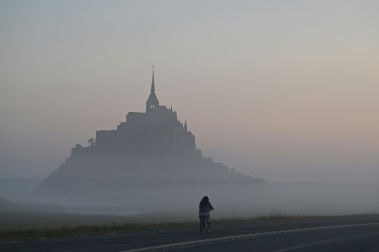 Un cycliste passe devant le Mont-Saint-Michel, enveloppé par la brume matinale, le 9 juillet 2025
